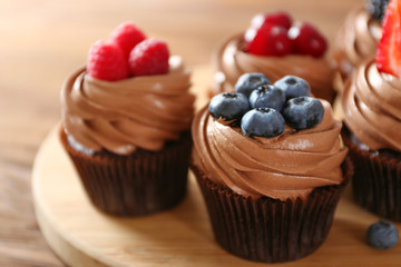 Tasty chocolate cupcakes with fresh berries on wooden mat