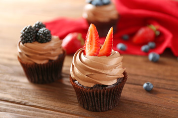 Tasty chocolate cupcakes with berries on wooden background