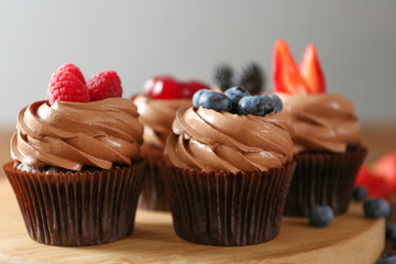 Tasty chocolate cupcakes with fresh berries on wooden mat