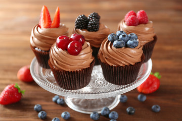 Tasty chocolate cupcakes with fresh berries on stand, wooden background