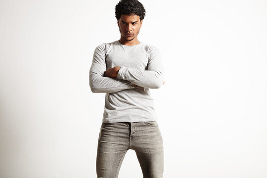 Sexy young African American man wearing light gray plain cotton longsleeve t-shirt and gray jeans with arms crossed looking slightly away from the camera with suspicion isolated on white.