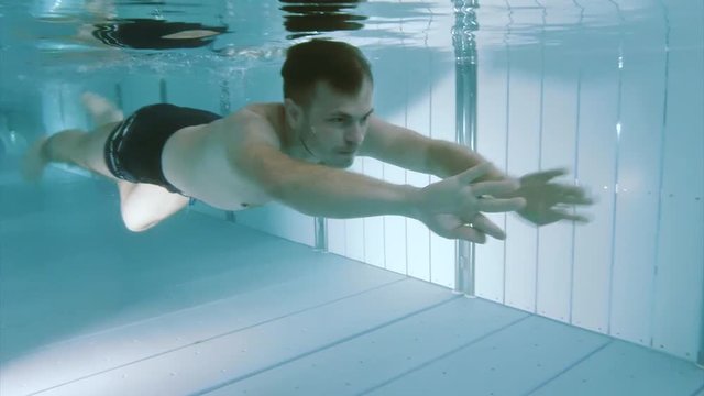 Underwater footage clip of young man swimming and diving in pool at aquapark.