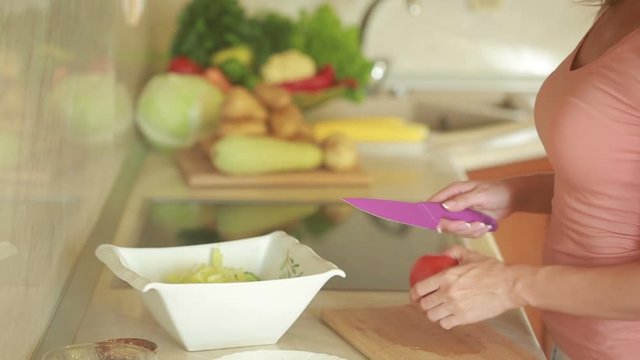 Young woman cutting vegetables in the kitchen for fresh salad. tomato