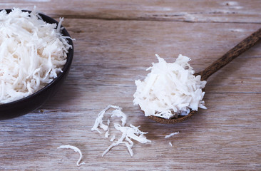 Spoonfull of shredded coconot on a wooden table.