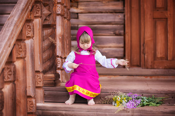 Masha on the porch of a wooden house with wildflowers