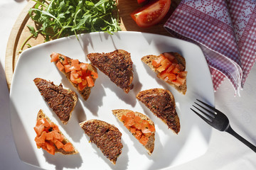 Brochette with tomato and olives on a white square plate, top view, horizontal, sunlit