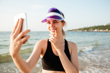 Smiling sporty woman taking selfie using smartphone on beach