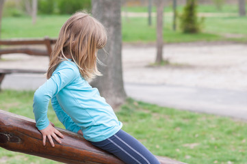 Little sad girl playing alone on the playground outdoor