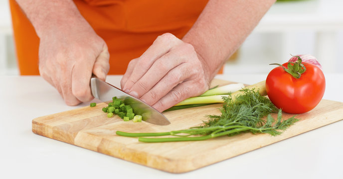 Man's hand with a knife cut  green onion on a wooden board.