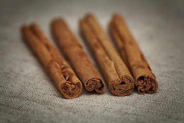 Cinnamon sticks on table with bundles of cinnamon in soft focus in background.  Selective focus limited to edges of closest sticks