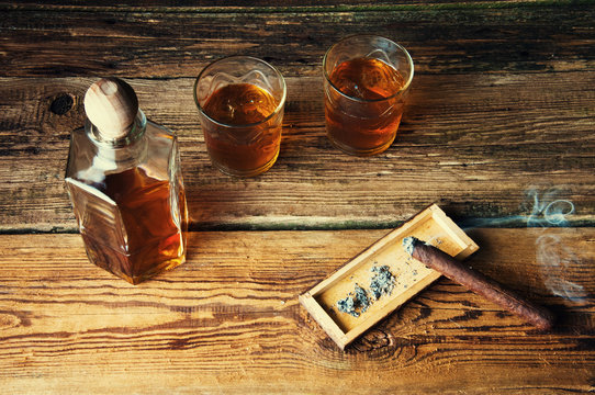 Cigar and whisky with ice on wooden table