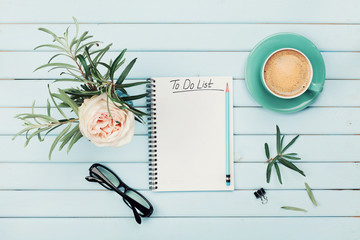 Morning coffee cup, notebook with to do list, pencil, eyeglasses and vintage rose flower in vase on...