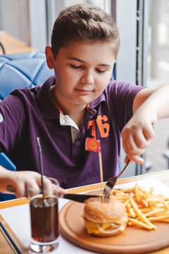 funny little boy eating a hamburger at a cafe, food concept