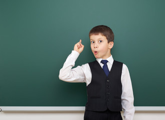 school student boy posing at the clean blackboard, show finger up and point, grimacing and emotions, dressed in a black suit, education concept, studio photo