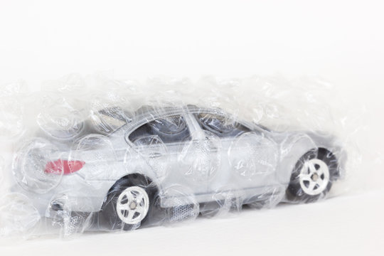 horizontal photo of a gray car toy with air bubble wrap on white