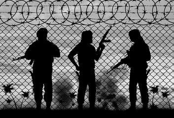 Silhouette of armed men against barbed wire fence