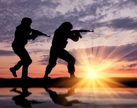 Silhouette of man aiming with rifle near border during sunset