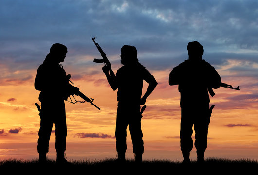 Silhouette of men holding rifles against cloudy sky during sunset