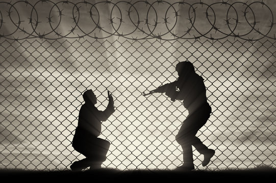 Silhouette of terrorist attacking on civilian near fence of barbed wire