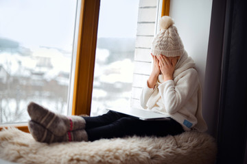 Cute girl with long hair sitting alone near window  with laptop