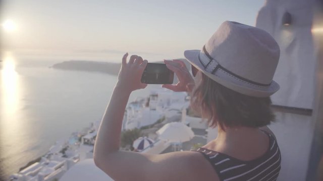 young woman tourist photographing the sunset on cell phone smartphone, in Greece, in Santorini