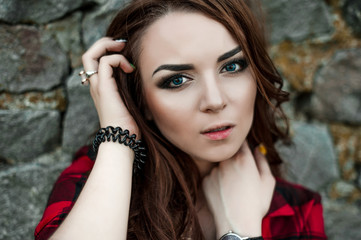 Obraz premium Beautiful young hipster girl posing and smiling near urban wall background in red plaid shirt, shorts, outdoors summer portrait.