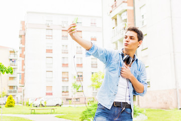 Young man in denim shirt and jeans taking a selfie outdoors in urban environment