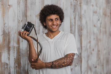 Portrait attractive and man with curly hair,holding a retro camera in his  hand and smiling, behind...