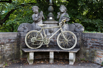 Fahrrad mit Schlamm steht auf einer Parkbank zusammen mit zwei  Steinfiguren