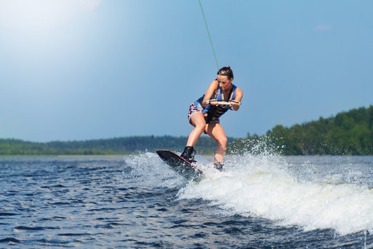 Slim brunette woman riding wakeboard on motorboat wave in lake