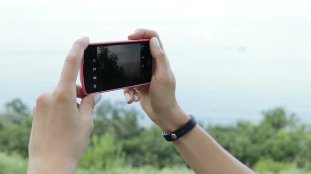 Female hands shoot video of the landscape on a mobile phone in summer