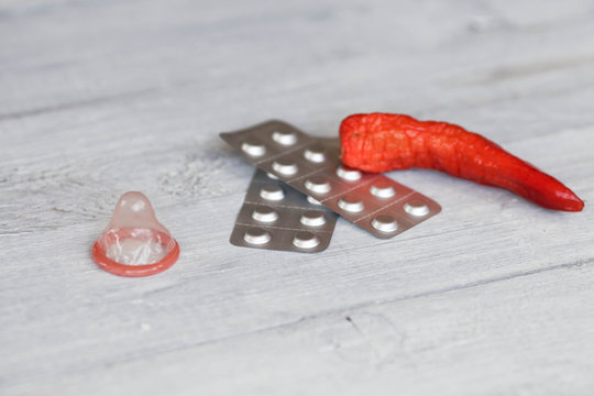 Condom, tablets and red pepper on a white wooden background