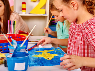 Group little girl and woman with brush painting on table in school. Painting box on foreground....