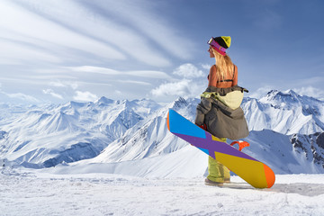 Back view of girl with colorful snowboard looking away mountains