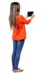 back view of standing young beautiful  woman  using a mobile phone. girl  watching. Rear view people collection.  backside view of person.  Isolated over white background. girl in a red jacket holding