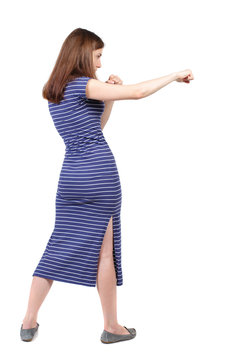 skinny woman funny fights waving his arms and legs. Isolated over white background. The brunette in a blue striped dress stands sideways and hit his foot.