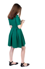 back view of standing young beautiful  woman using a mobile phone or tablet computer. girl  watching. Rear view people collection.  backside view of person.  Isolated over white background. The