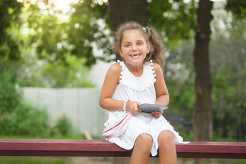 Laughing girl sitting on the bench and playing tablet . She is d
