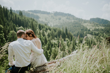 Naklejka premium Vintage wedding photography of a young hipster couple curly bride posing at sunset in the forest and mountains dressed in a suite and white dress