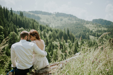 Fototapeta na wymiar Vintage wedding photography of a young hipster couple curly bride posing at sunset in the forest and mountains dressed in a suite and white dress