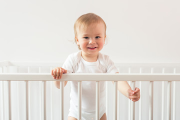 Portrait of a laughing baby standing in a crib and looking at the camera.