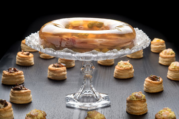 Alzatina di cristallo con aspic tra i vol-au-vent ripieni su un tavolo nero