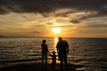 A child with his parents standing on sea beach and watch the sunset