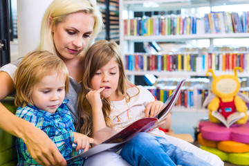 Mother with little girl and boy read book together in library
