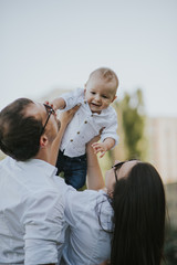 Happy young family having fun, bowl, rising up, piggyback ride their child in park on summer sunset
