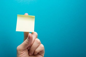 Sticky note, finger up of thumb, yellow reminder on blue background.