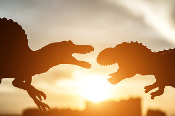 silhouette of spinosaurus and tyrannosaurus with buildings in far end in sunset time