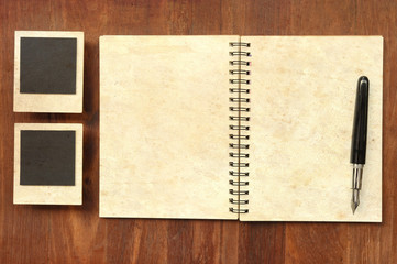 Blank notebook with pen and photo frames on wooden background with sunlight vintage color