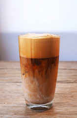 Close up of a glass of iced milk coffee on a wooden table.