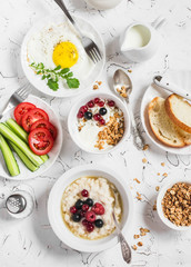 Table breakfast - cottage cheese with yogurt and berries, oatmeal with honey and berries, fried egg, fresh vegetables,  homemade granola on a light background. Healthy food. Top view